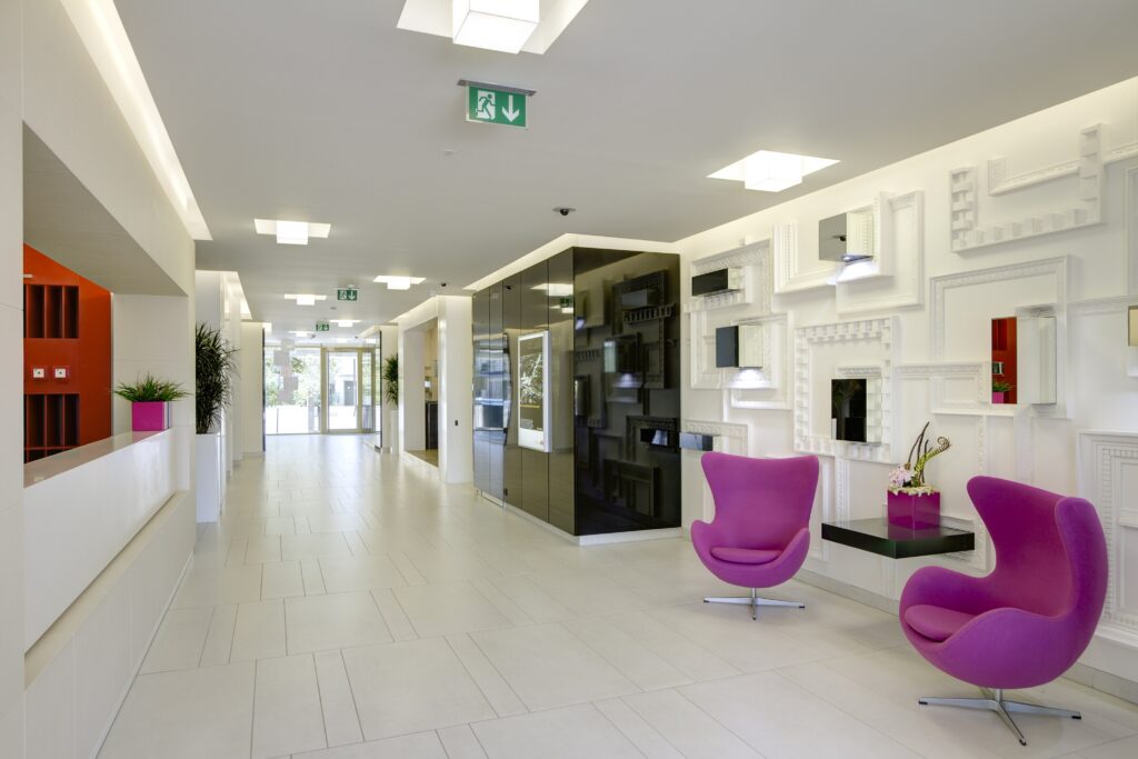 Revitalisiertes Bürogebäude Qubix in Prag – modernes Interieur mit heller Lobby, Designwand und farbigen Sitzmöbeln, entworfen von TMLC Architects, Architekten Martin Troethan und Clemens Liedermann-Seiss